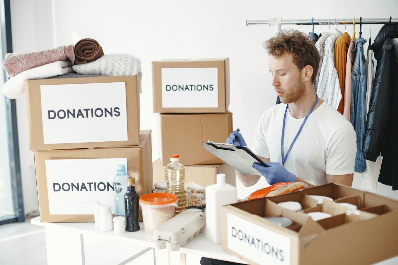 services-02 A man organizing donation boxes filled with clothes and food items at an NGO office.